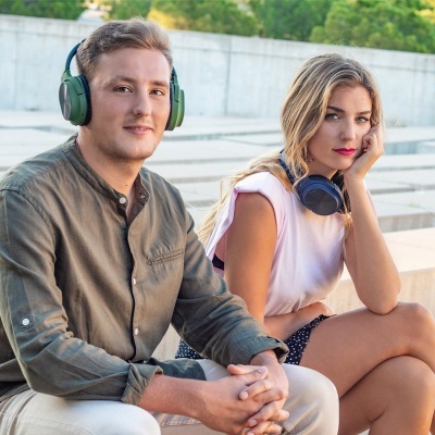 Homem e mulher sentados com auscultadores grandes, camisa verde e top branco em espaço exterior