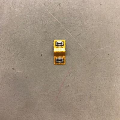 Componente eletrónico flexível amarelo com duas partes metálicas prateadas sobre superfície cinzenta