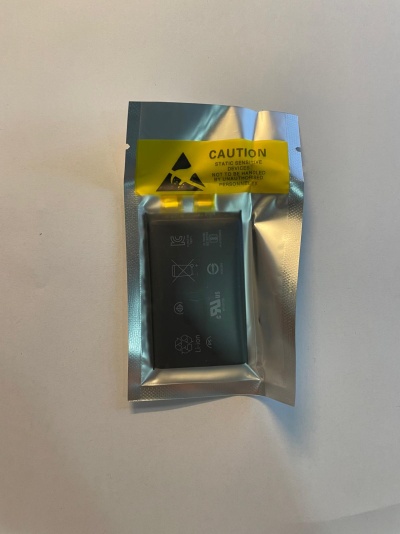 Bateria preta embalada em saco prateado com etiqueta amarela de aviso