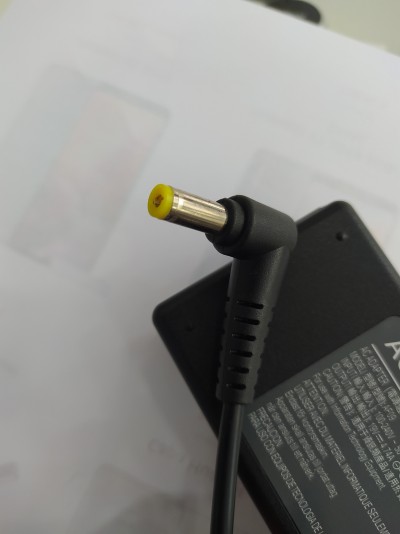 Adaptador de alimentação preto com conector de ponta amarela sobre papel