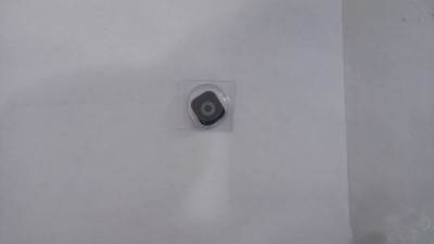 Objeto hexagonal preto com círculo cinza em embalagem plástica sobre fundo branco