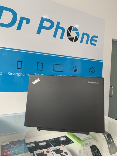 Computador portátil Lenovo preto inclinado em superfície de vidro com cartaz Dr Phone ao fundo