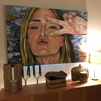 pintura de mulher loira com mão fazendo sinal de paz, móvel com lâmpada, castiçais, caixas decorativas e cerâmica