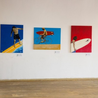 Parede branca com quatro quadros pequenos coloridos representando figuras humanas a surfar e andar de bicicleta na praia.