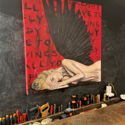 Quadro vermelho com figura feminina e asa negra na parede preta sobre bancada de ferramentas