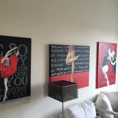 Três quadros artísticos de bailarinas em parede branca, com sofá e lâmpada à frente