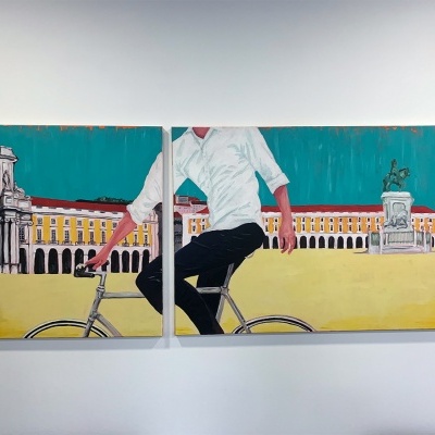 Pintura abstrata de pessoa de camisa branca numa bicicleta frente a edifícios amarelos