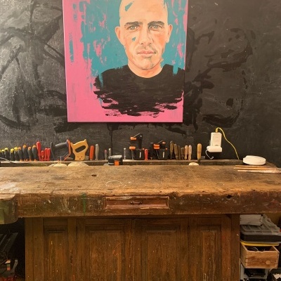 Bancada de madeira com ferramentas e quadro de retrato colorido numa parede escura