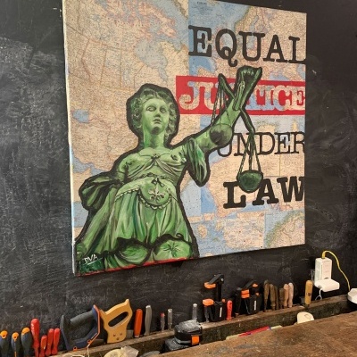 Tela com pintura da estátua da justiça e texto sobre mapa em parede preta
