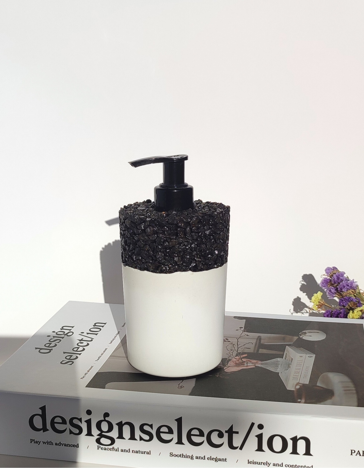 Dispensador de Sabão Branco Rio S Dispenser de sabonete branco com topo preto texturizado sobre livro design selection com flores ao fundo