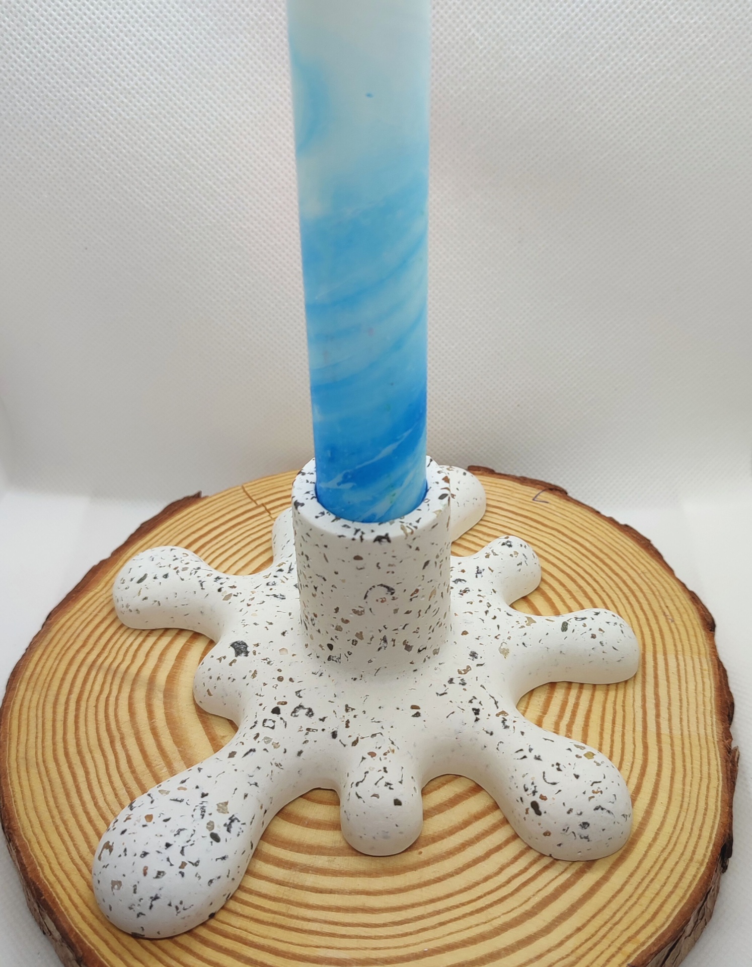 Castiçal Água Fluída Castiçal branco com manchas coloridas e vela azul com padrão espiral sobre base redonda de madeira