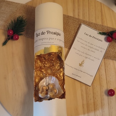 Vela branca com presépio em concha e cartão com texto sobre luz do presépio, sobre placa de madeira circular