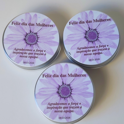 Três latas metálicas com tampa decorada com flor roxa e texto comemorativo em português.