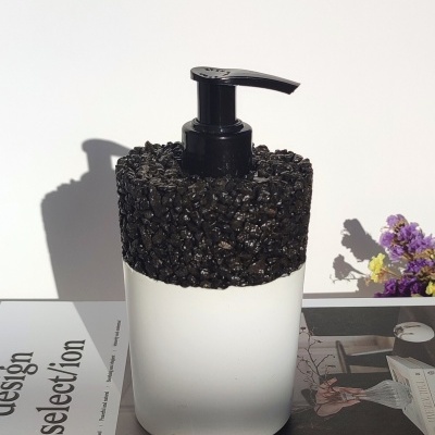 Frasco branco com tampa preta texturizada e bomba, em superfície branca, com flores ao lado.