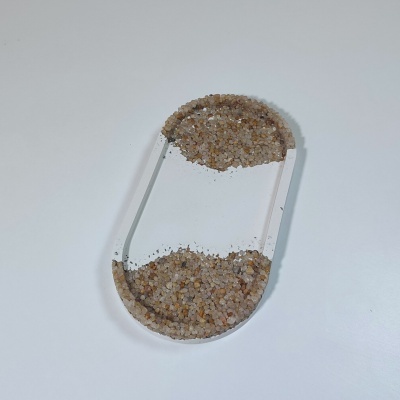 Acessório transparente em forma de pílula com areia castanha dentro