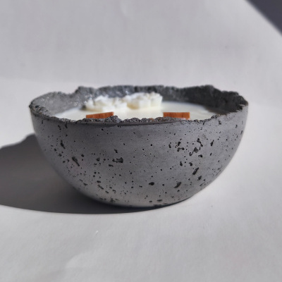 Vela branca em recipiente cinza de cimento com pavios de madeira