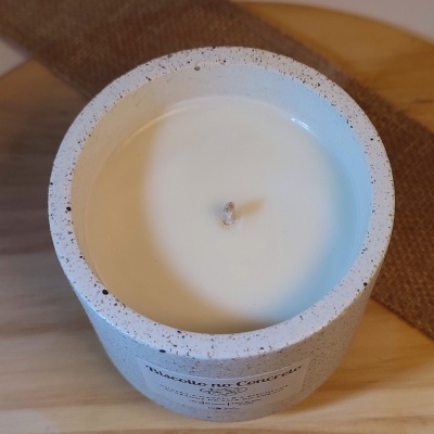 Vela branca em base de cimento cinza com textura pontilhada preta sobre superfície de madeira clara
