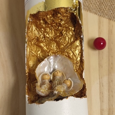 Escultura decorativa com bonecos em conchas e dourado, embalagem branca com texto e fundo de madeira