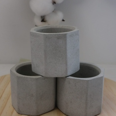 Três vasos cinzentos de cimento com design facetado empilhados sobre uma superfície de madeira