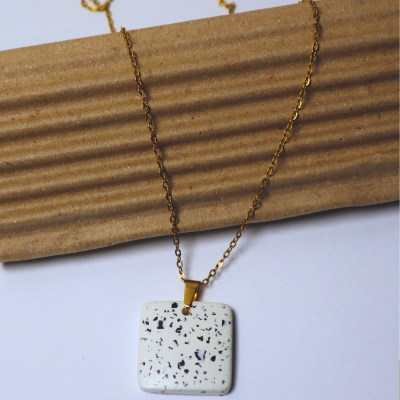 Colar dourado com pendente branco com manchas pretas sobre cartão ondulado castanho