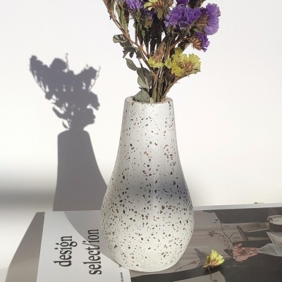 Vaso de cerâmica branca com manchas e flores secas sobre livro 'design selection'