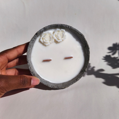 Vela branca em tigela cinzenta com flores brancas decorativas e dois pavios.