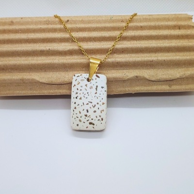 Colar dourado com pendente branco com manchas douradas sobre cartão ondulado