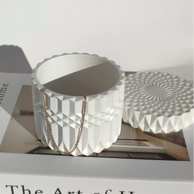 Caixa decorativa branca com padrão geométrico e corrente dourada sobre livro 'The Art of Home'