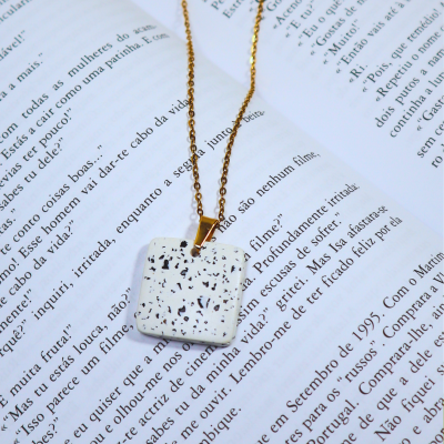 Colar com pendente quadrado branco com manchas pretas sobre livro aberto