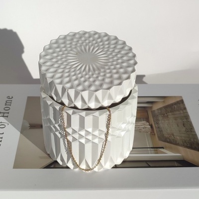 velas perfumadas brancas com padrão facetado em tampa decorada e base, sobre livro THE ART OF HOME