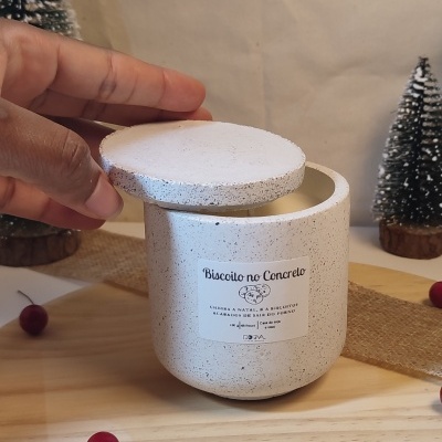 Vela perfumada em recipiente de concreto cinza claro com etiqueta e decoração natalícia.