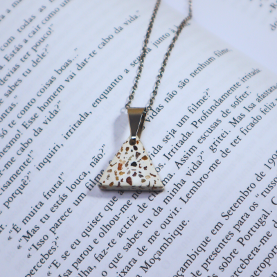 Colar com pendente triangular em pedra branca manchada sobre livro aberto