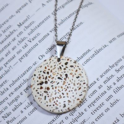 Colar com pendente redondo branco e padrão manchado castanho sobre página de livro.