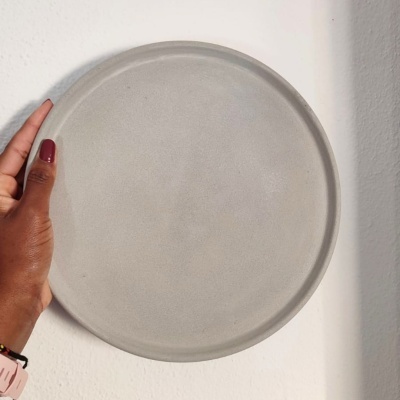 Prato redondo cinzento claro com textura lisa segurado por uma mão