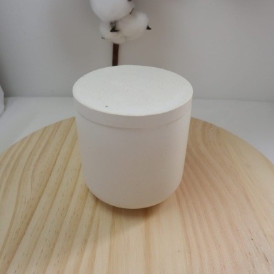 Frasco branco cilíndrico com tampa sobre placa de madeira clara e ramo de algodão ao fundo