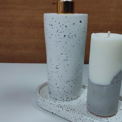 Frasco dispensador branco com padrão salpicado preto e vela branca em bandeja oval.