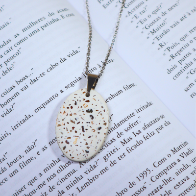 Colar com pendente oval branco salpicado sobre livro aberto