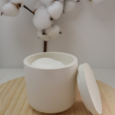 Recipiente branco aberto com pó branco e ramo de algodão em fundo neutro