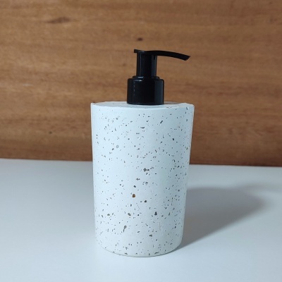 Dispenser de sabão líquido branco pontilhado com tampa preta sobre superfície branca e fundo madeira.