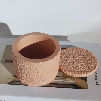 Recipiente redondo em terracota texturizada com tampa, sobre um livro.