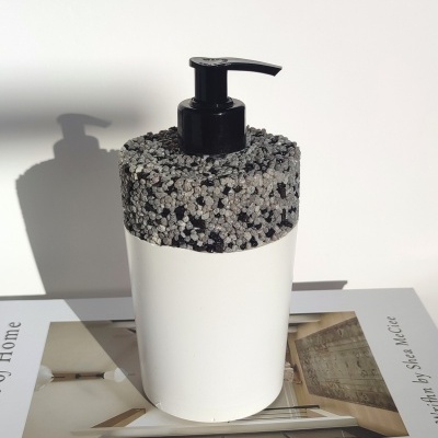 Dispenser de sabão branco com tampa de textura em pedras cinzentas e pretas sobre livro de decoração