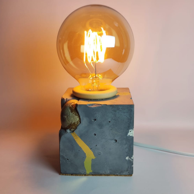Lâmpada de filamento numa base cúbica de cimento com detalhes dourados