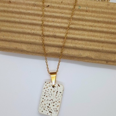 Colar dourado com pendente branco com manchas castanhas sobre fundo branco e cartão