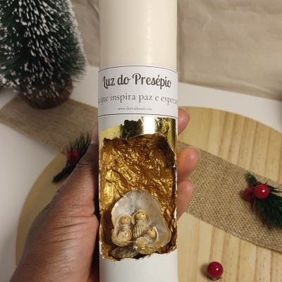 Vela branca decorativa com presépio feito de conchas e papel dourado