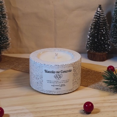 Vela em recipiente de concreto redondo com etiqueta em superfície de madeira e decoração natalícia