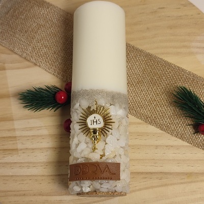 Vela branca decorada com pedras e peça dourada sobre tábua de madeira redonda