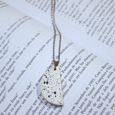 Colar prateado com pendente branco com manchas pretas sobre livro aberto