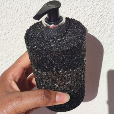 Frasco doseador preto texturizado com tampa de dispenser segurado por uma mão