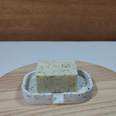 Sabonete creme com partículas numa saboneteira branca com manchas negras sobre base de madeira