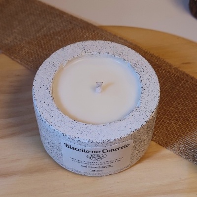 Vela branca num recipiente cilíndrico cinzento com etiqueta Biscoito no Concreto